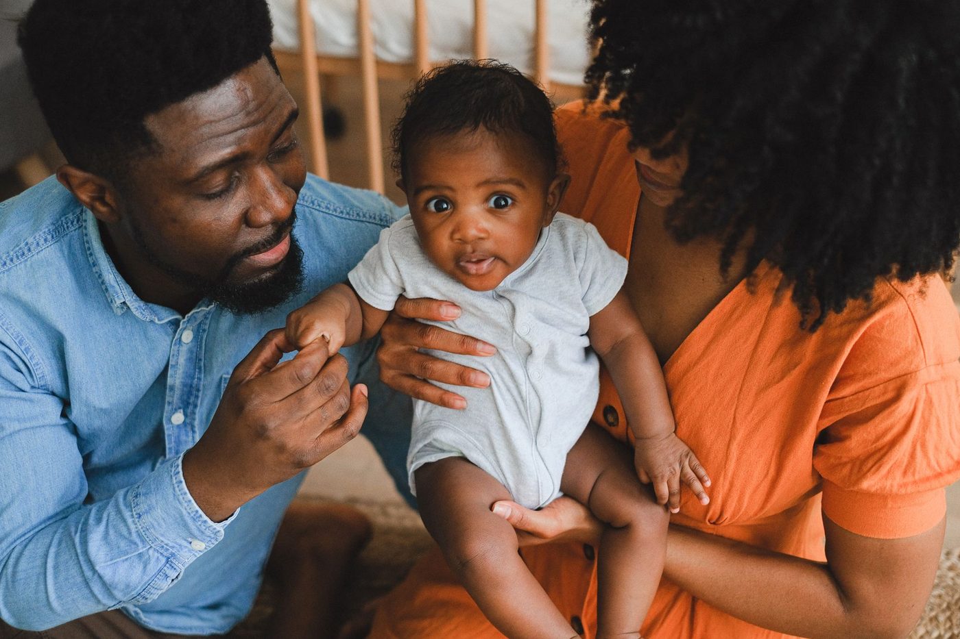 Parents holding a baby in a gray onesie at home